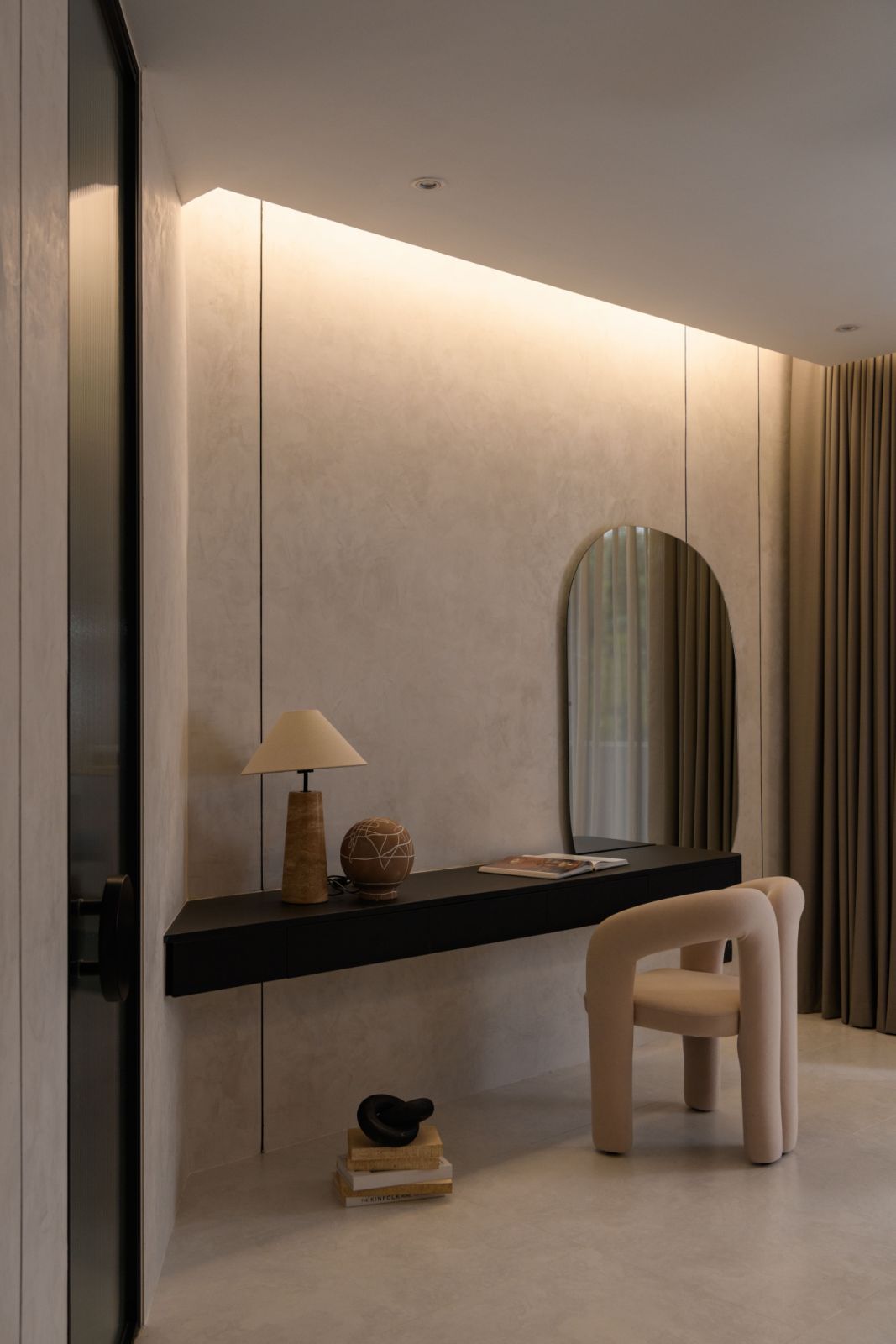 Continuing the home’s signature curved aesthetic, an organically shaped mirror and sculptural vanity chair create a soft, feminine counterpoint