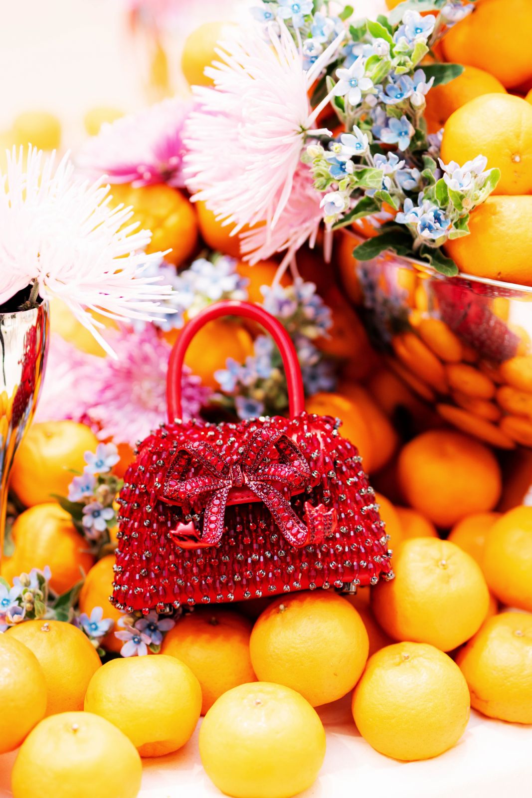 Red bejewelled Self-Portrait handbag with ribbon photographed against oranges
