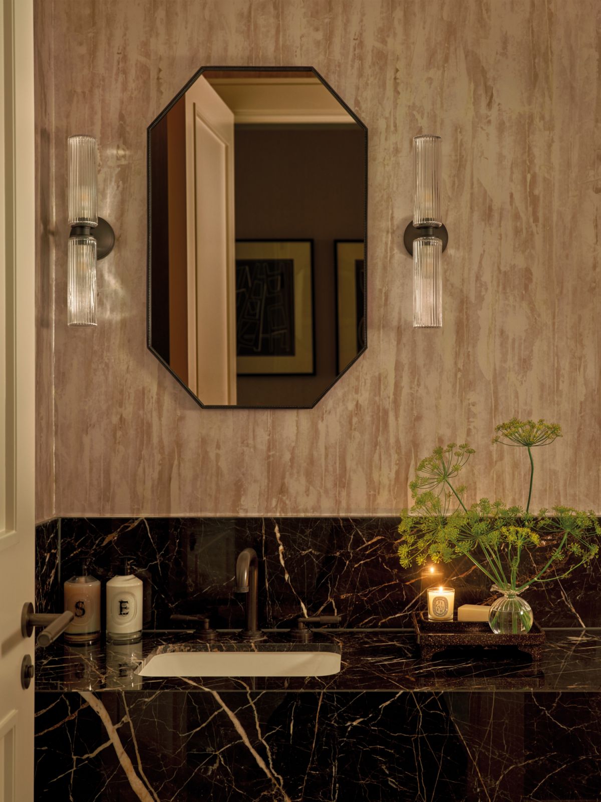 In this sumptuous bathroom, a striking octagonal mirror elegantly complements the dark marble surfaces, creating a luxurious atmosphere that exudes sophistication and style