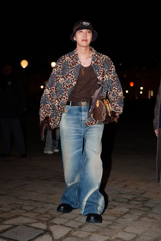 PARIS, FRANCE - JANUARY 21: J-Hope wears a bob hat, a colored checkered pattern oversize blazer jacket , a brown t-shirt, a brown leather monogram logo print bag from Louis Vuitton , flared wide leg denim pants / jeans , black leather shoes, before the Louis Vuitton Menswear Fall-Winter 2025/2026 show as part of Paris Fashion Week on January 21, 2025 in Paris, France. (Photo by Edward Berthelot/Getty Images)