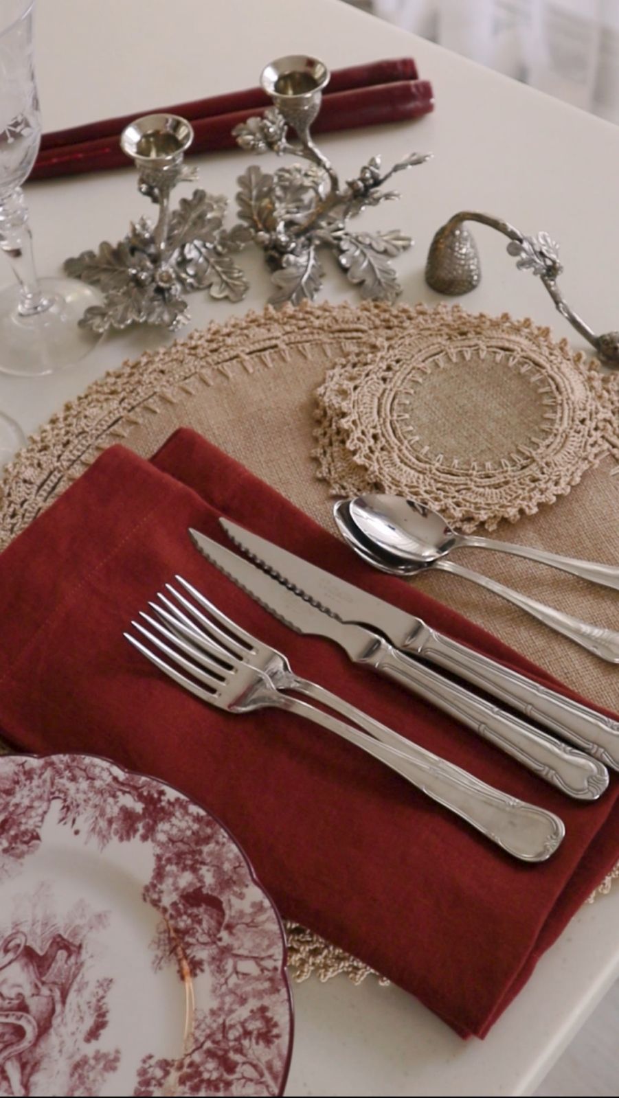 Vintage-inspired toile salad plates from Dior and silver ornamental candleholders from a flea market in Paris with neutral crochet placemats and coasters from Cabana Workshop, silver flatware, and folded linen napkins from Crate & Barrel