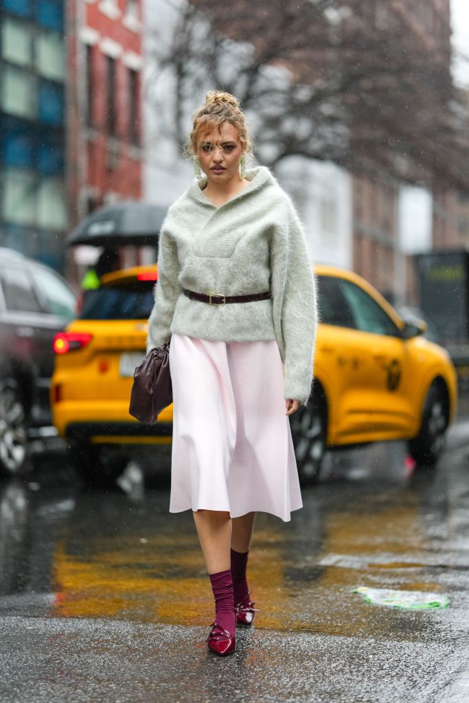 NEW YORK, NEW YORK - FEBRUARY 06: A guest wears muted green fluffy oversized sweater, shiny black leather belts, shiny dark brown leather bag, light pink midi skirt, burgundy bordeaux socks, shiny burgundy bordeaux pointed toe kitten heels leather shoes, outside Brandon Maxwell, during the New York Fashion week Fall/Winter 2025 on February 6, 2025 in New York, New York. (Photo by Edward Berthelot/Getty Images)