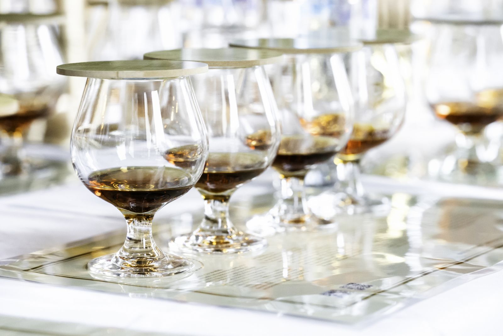 Close up of row transparent drinking glasses with rum on the tasting placemats. Event for connoisseurs of blended old aged strongest liquors. High quality photo
