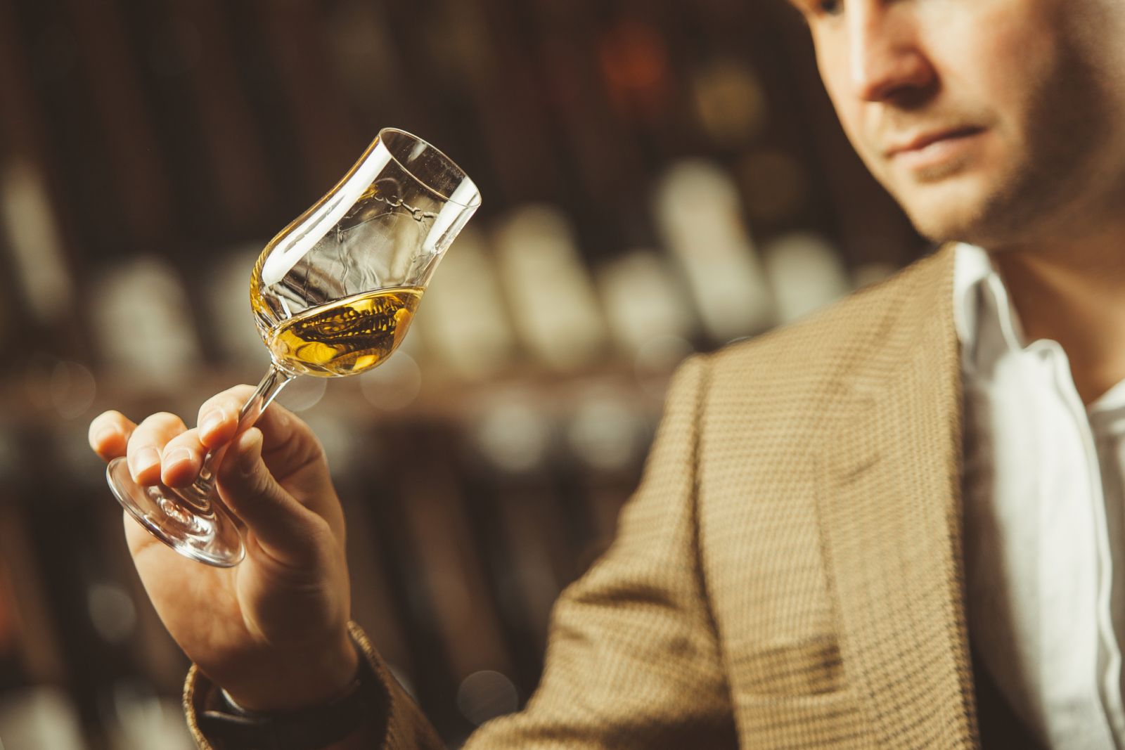 Bokal of whiskey on background of male sommelier appreciating color, quality, flavor and sediments of drink. Professional degustation expert in whiskey making.