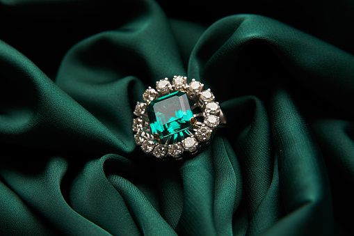 Green emerald fashion engagement diamond ring on green satin background. Luxury female jewellery, close-up. Selective focus