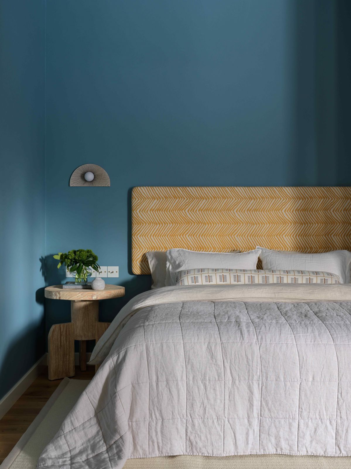 The upholstered headboard in inca gold against a bright blue backdrop