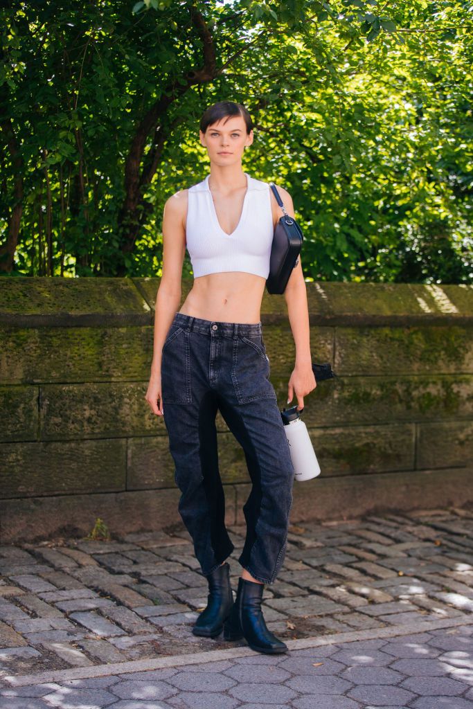 NEW YORK, NEW YORK - SEPTEMBER 10: Model Cara Taylor wears a white fitted croptop, black purse, black two-tone jeans, black booties, and carries a white Hydro Flask water bottle after the Michael Kors show on September 10, 2021 in New York City. (Photo by Melodie Jeng/Getty Images)