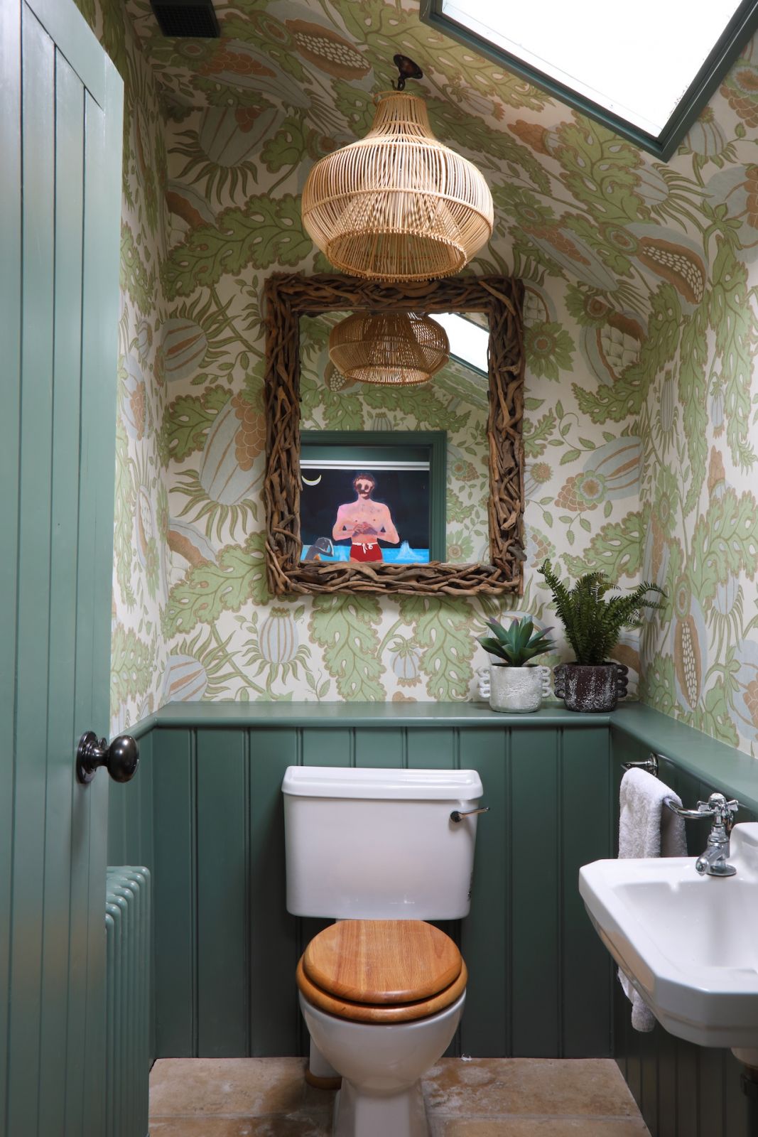 The guest bathroom of a Sussex, England home painted a teal shade that complements the playful, forest-themed wallpaper