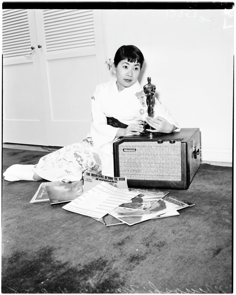 Miyoshi Umeki (with Oscar), 3 April 1958. Miyoshi Umeki (with Oscar) Negatives for picture living.;Caption slip reads: 'Photographer: Lou Mack. Date: 1958-04-03. Assignment: Parsons, pic. Living. Miyoshi Umeki, with Oscar, negs. for pic. living. One neg. Miyoshi holds sheet music titled, 'The Man I Love' with Oscar in foreground, by piano'.. (Photo by Los Angeles Examiner/USC Libraries/Corbis via Getty Images)