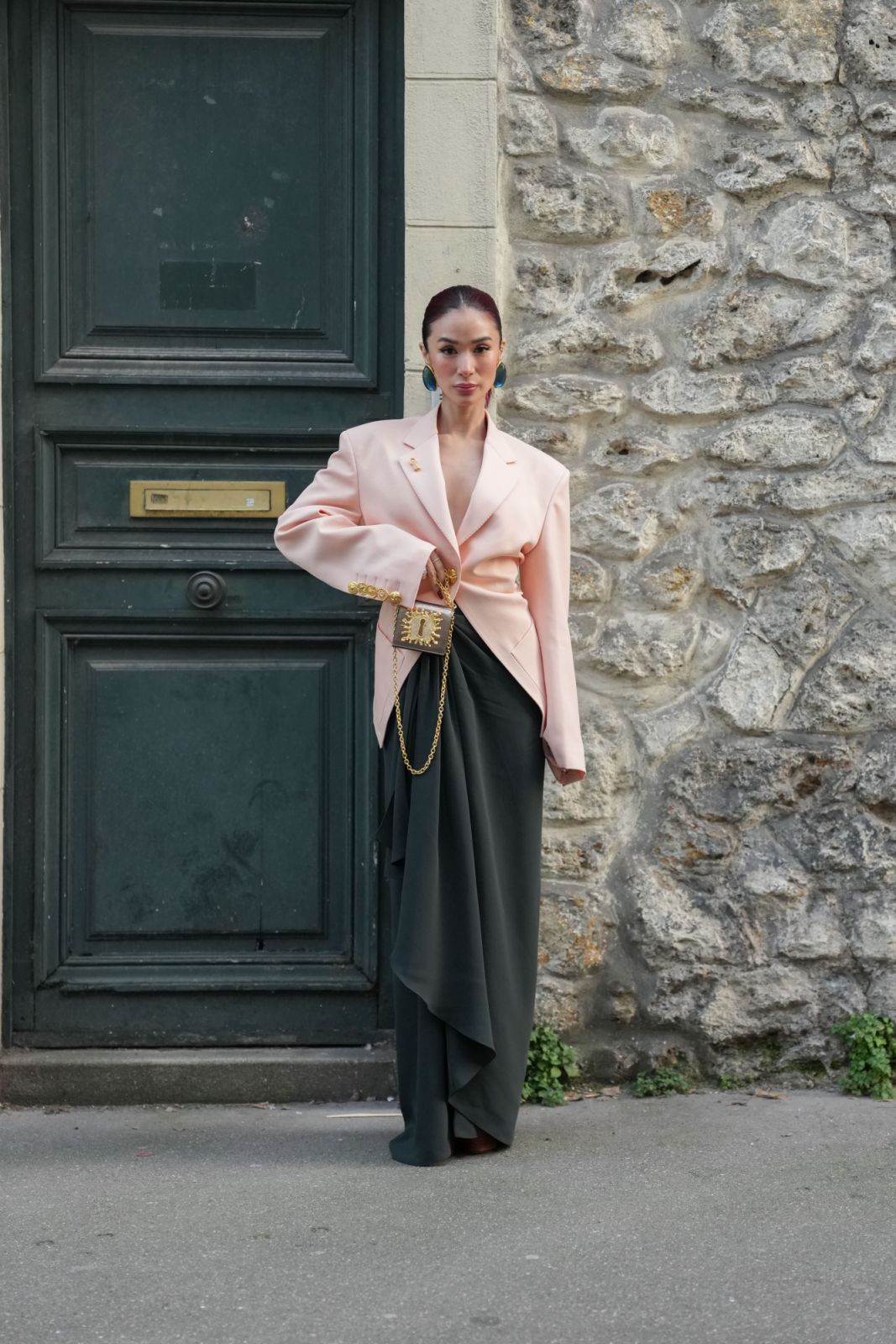 Heart Evangelista wears Schiaparelli earrings, a light pink gold-buttoned detail oversized Schiaparelli blazer jacket, a black draped midi skirt, a black and gold detail Schiaparelli Keyhole leather bag, and dark brown platform heels leather shoes outside Schiaparelli during their Women's Fall/Winter 2025-2026 show (Photo: Edward Berthelot/Getty Images)