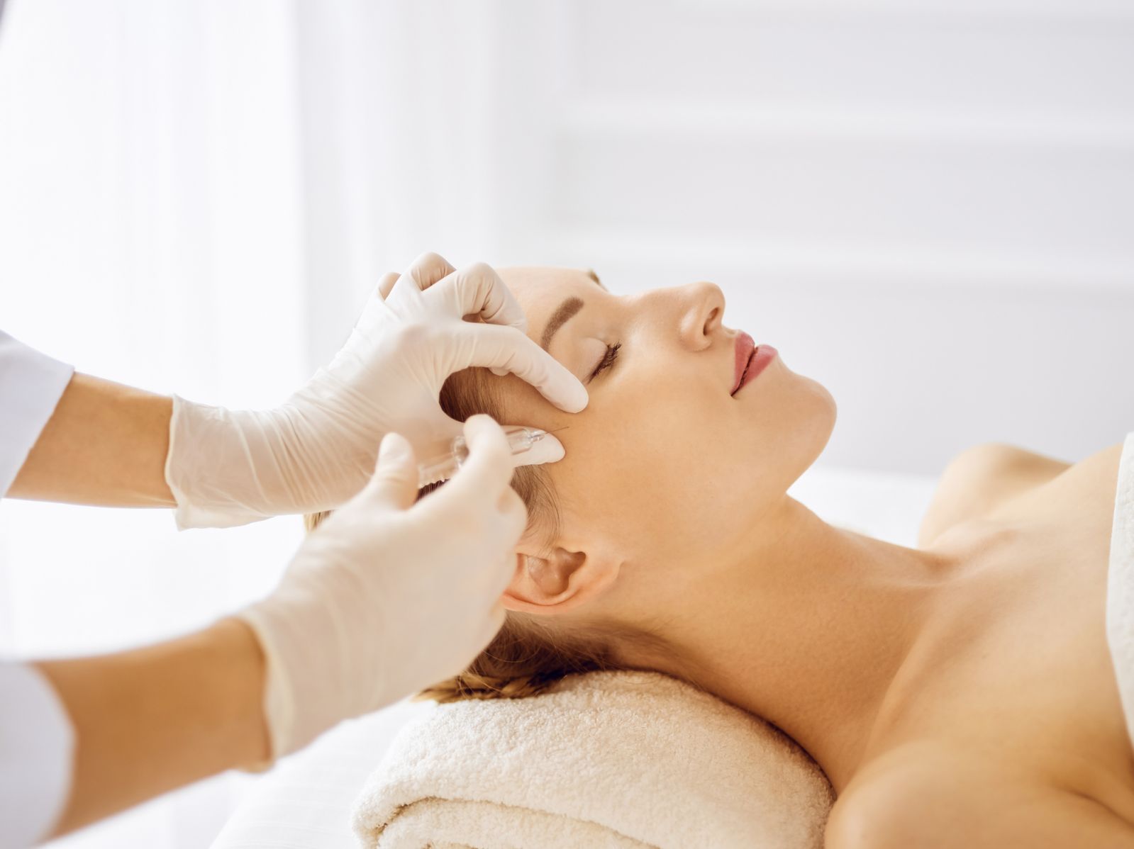 Beautiful woman receiving beauty injections with closed eyes. Beautician doctor hands doing beauty procedure to female face with syringe. Cosmetic medicine and surgery concept.