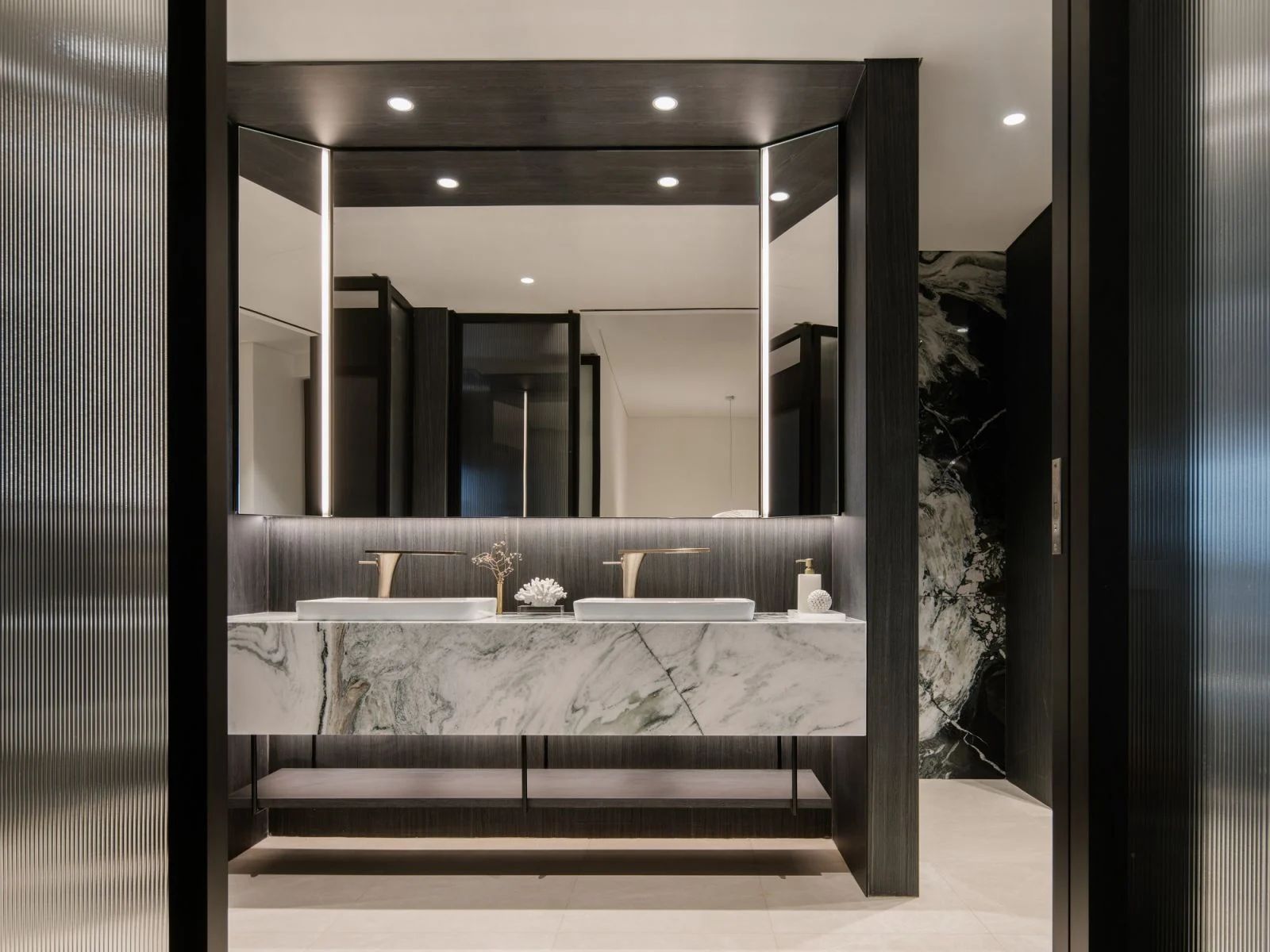 The bathroom contrasts darker structural elements with striking light-toned marble surfaces
