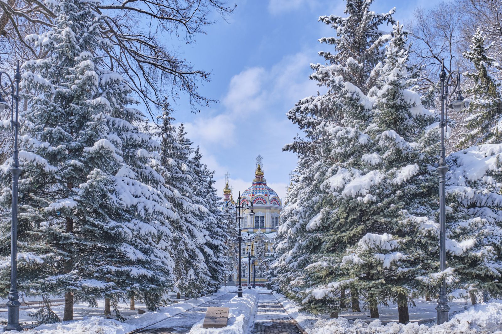 Snowy alley in Park named after 28 Panfilov guardsmen, Almaty, Kazakhstan. Ascension Cathedral, Russian Orthodox wood cathedral. Translation for non-English text: Alley of Heads of State