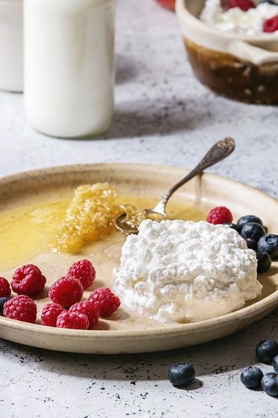 Piring keramik berisi keju cottage buatan sendiri, disajikan dengan blueberry, raspberry, sebotol susu, dan honeycomb di atas meja bertekstur marmer putih sebagai latar belakang (Photo by: Natasha Breen/REDA/Universal Images Group via Getty Images)