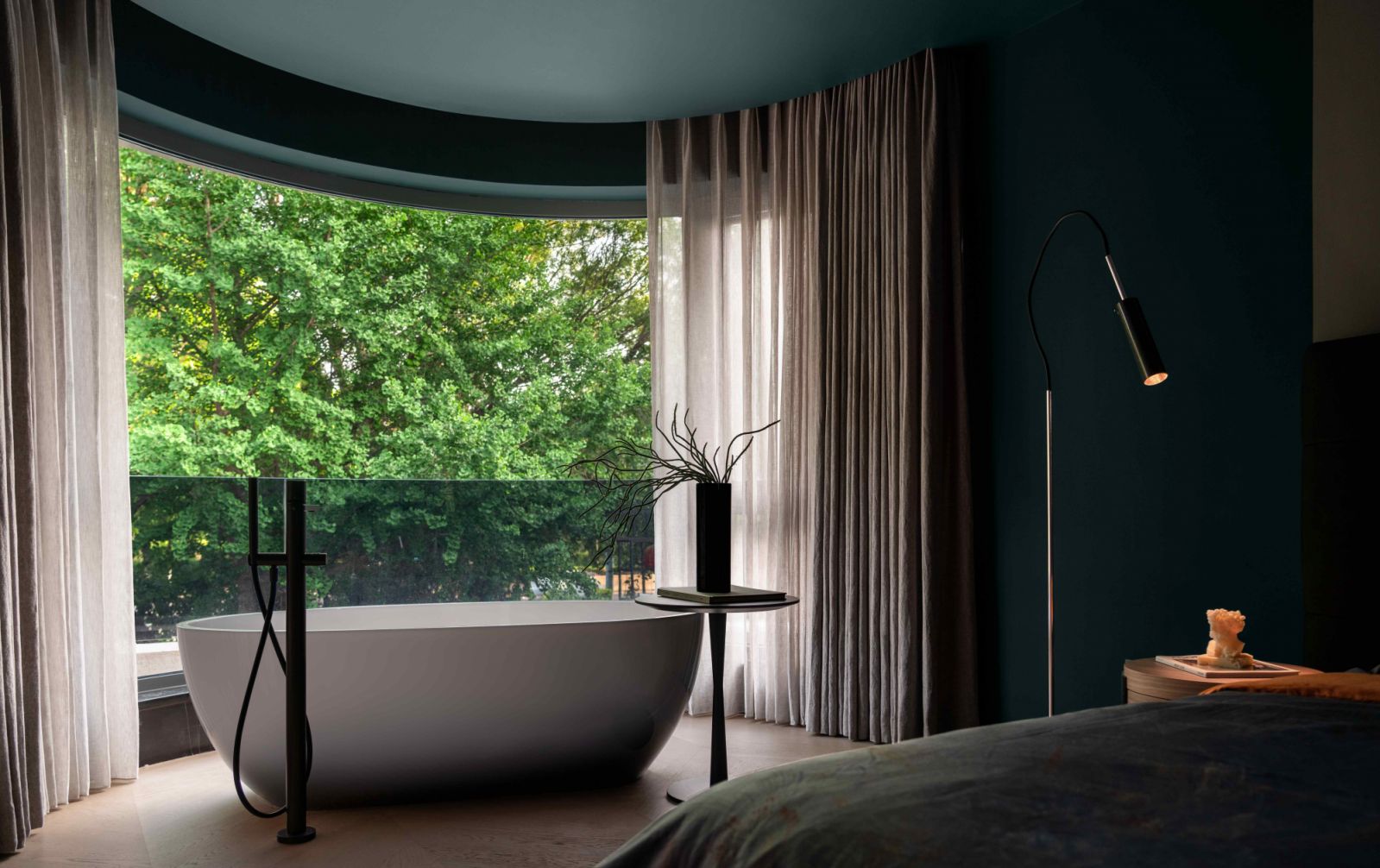 The freestanding bathtub sits before a large curved window to offer views of the rear garden below