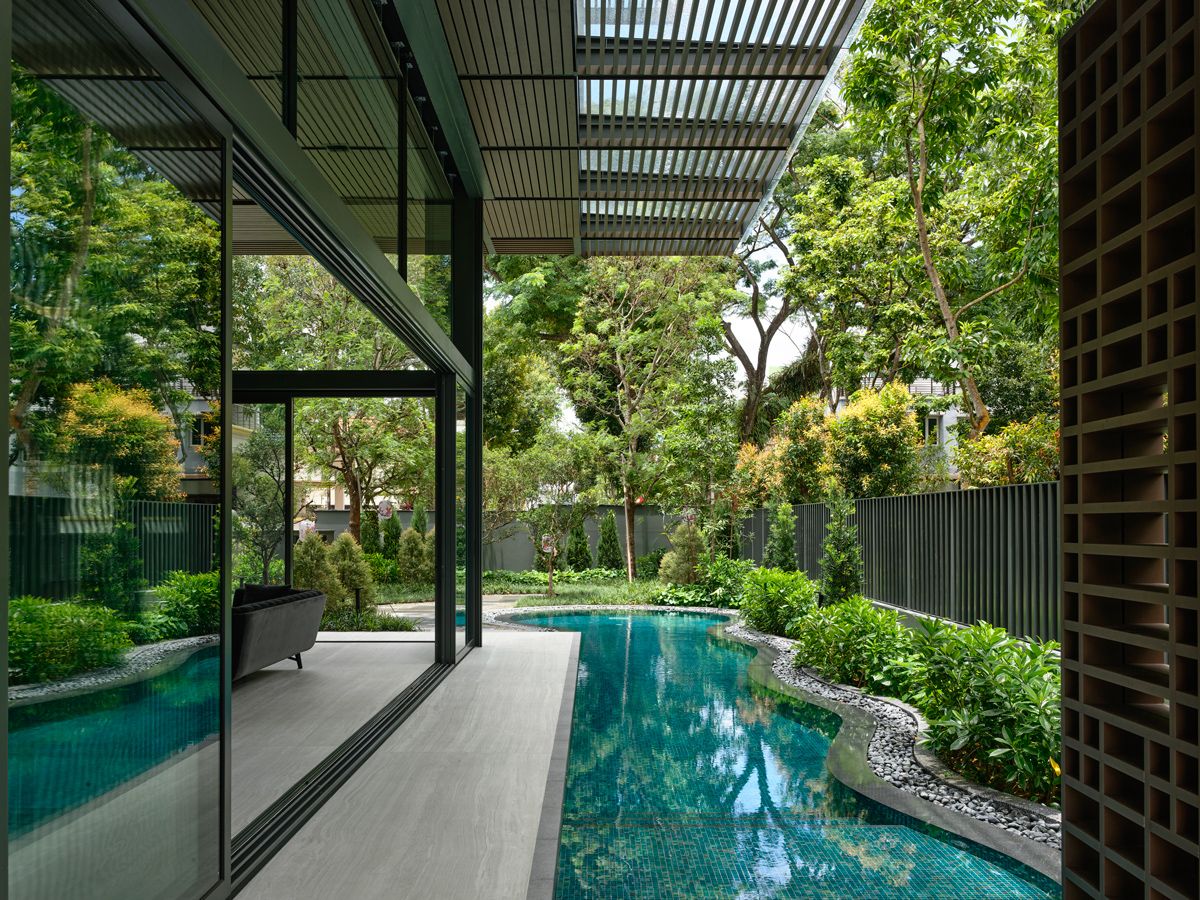 The house's glazed front reflects the surrounding lush greenery