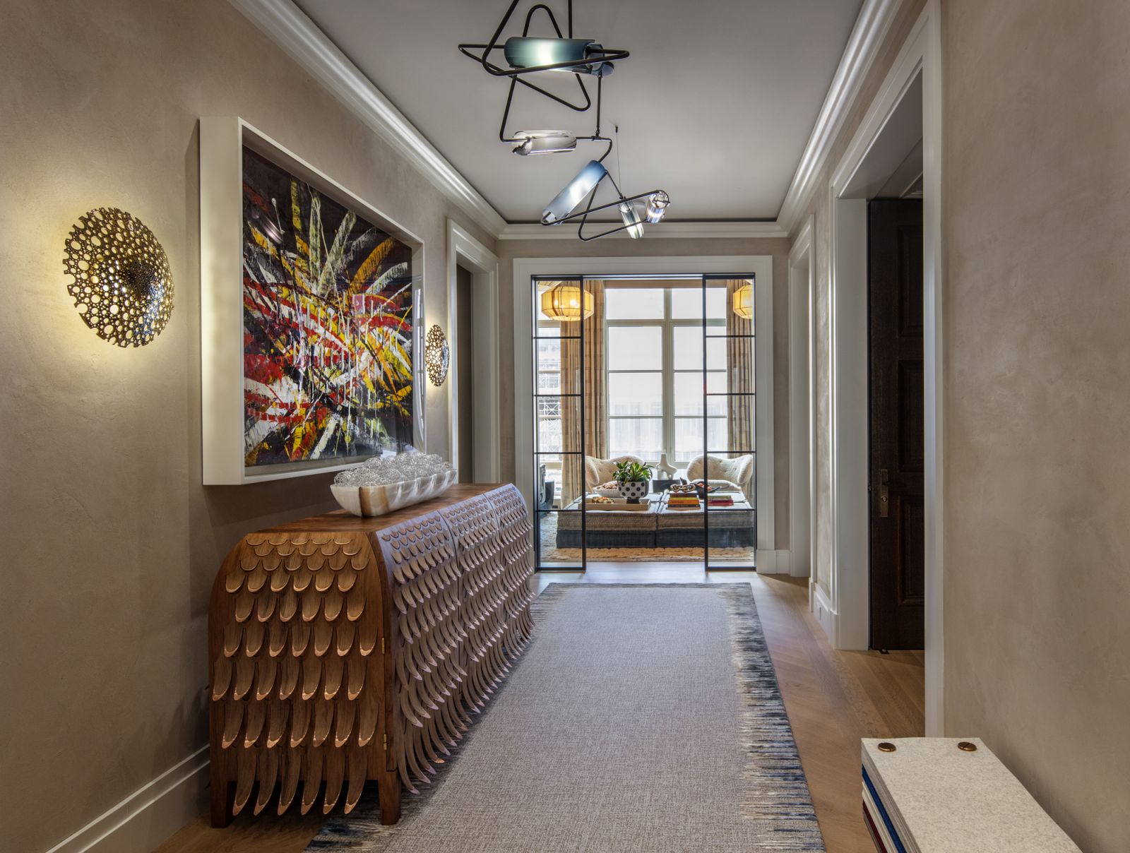 The gallery in the entryway of the home, with a side view of the Pankalangu Credenza by Trent Jansen via Gallery All and the artwork “Untitled (Capri 53, 18)” by Mark Grotjahn beneath a chandelier by Avram Rusu Studio