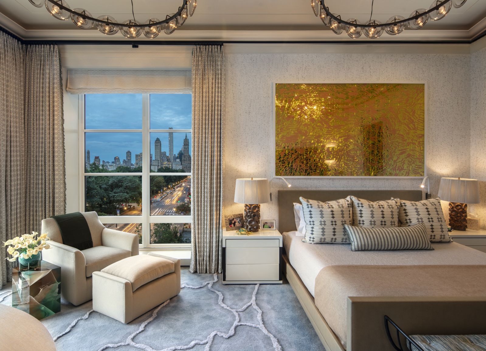 The primary bedroom with a bed by Joseph Jeup, upholstered in a Skintex faux ostrich leather and pillows in a Holland & Sherry silk hand-block print, chandeliers from Ochre in a Central Park, New York family home