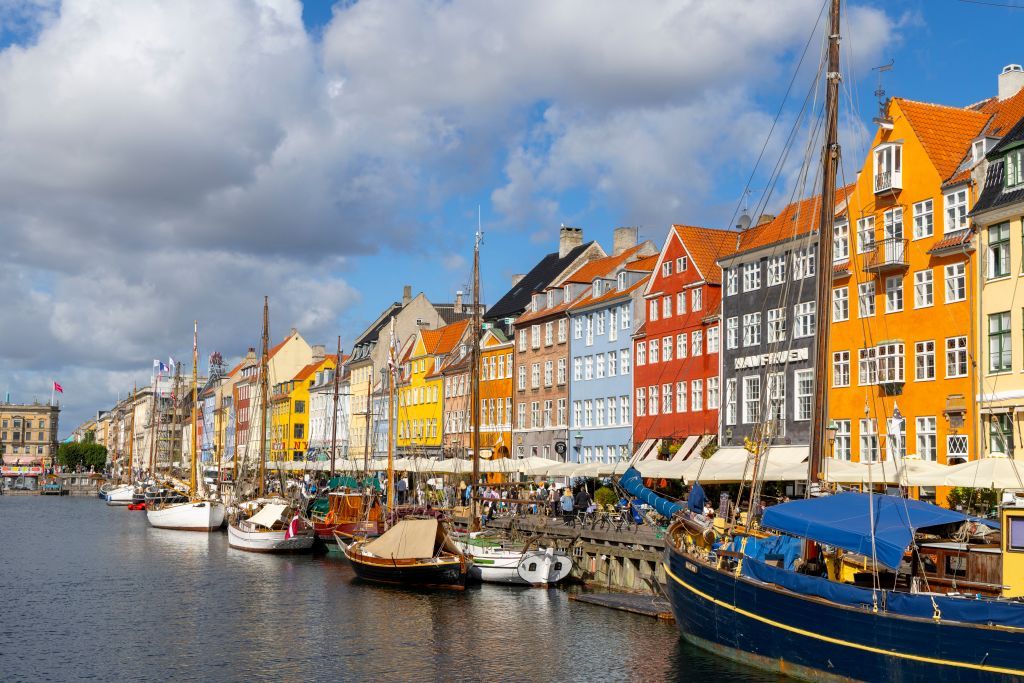 Copenhagen entertainment and restaurant scene beside the canal in Nyhavn district with boats along the canal and people enjoying a restaurant lunch in front of the colored townhouses. (Photo by: Martin Berry/UCG/Universal Images Group via Getty Images)