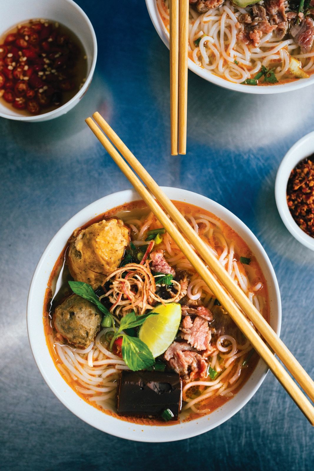 High angle close up of bowl of Bun Bo Hue with beef, crab balls, blood sausage and herbs.