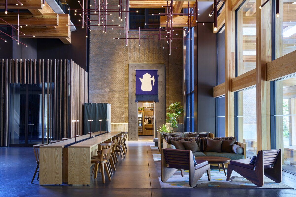 Double-height communal space at Ace Hotel Kyoto designed by Kengo Kuma, featuring exposed timber beams, minimalist lighting, and angular mid-century seating (Photo: Ace Hotel Kyoto)