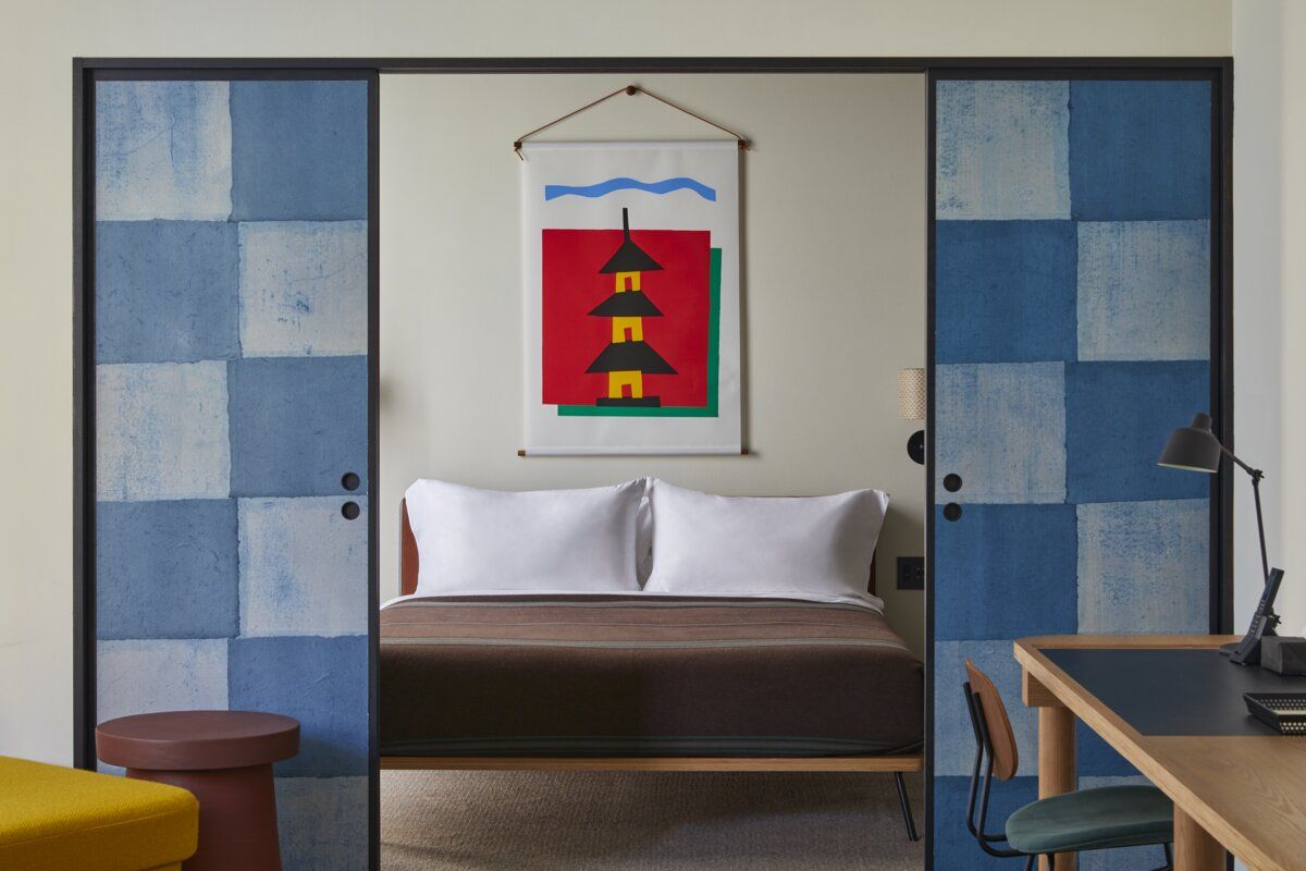 Guest room at Ace Hotel Kyoto with indigo-dyed sliding doors and graphic art depicting Japanese architecture, blending traditional craft with mid-century aesthetics (Photo: Ace Hotel Kyoto)