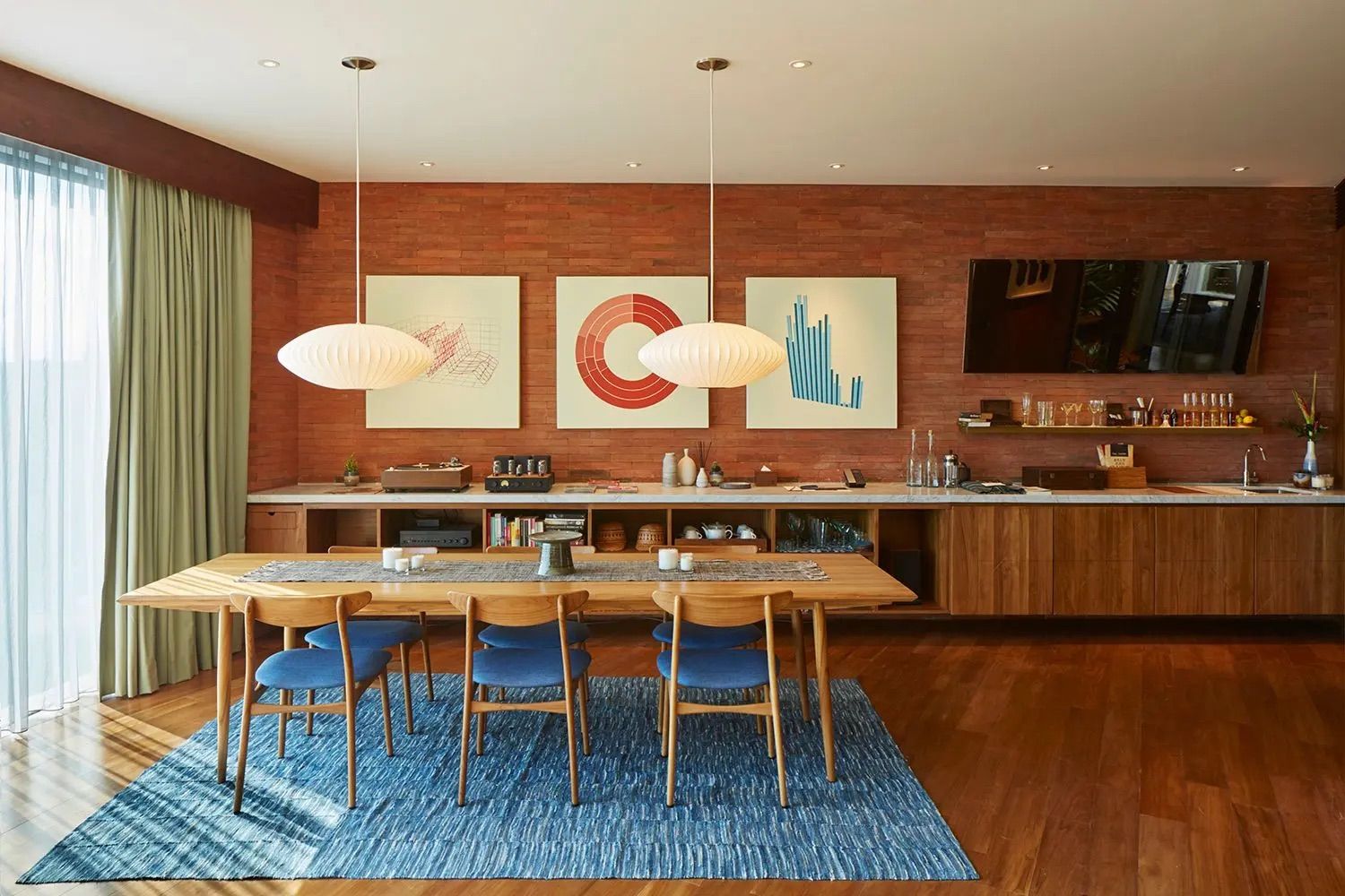 Dining area in Katamama Bali featuring handcrafted teak furniture, George Nelson-inspired pendant lamps, and geometric artwork against textured brick walls—a perfect example of tropical modernism (Photo: Katamama Bali)