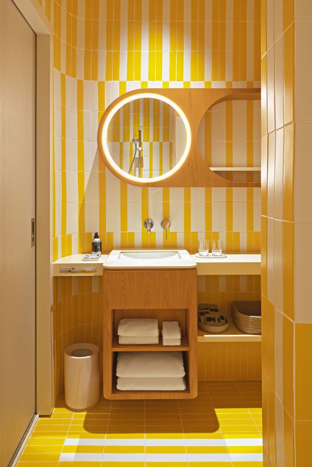 Vibrant mid-century inspired bathroom at The Standard Singapore featuring geometric yellow and white tiled walls, wood cabinetry, and circular illuminated mirror (Photo: The Standard Singapore)