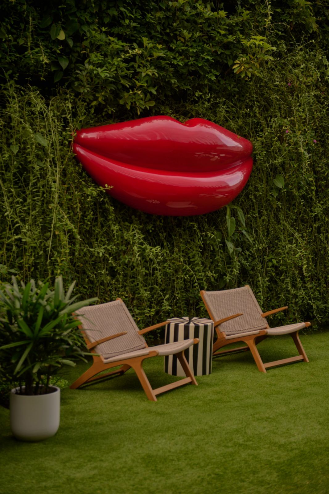 Garden seating area at The Standard Singapore featuring sculptural red lip installation, wooden lounge chairs, and lush vertical planting—illustrating the hotel's playful take on modernist outdoor spaces (Photo: The Standard Singapore)