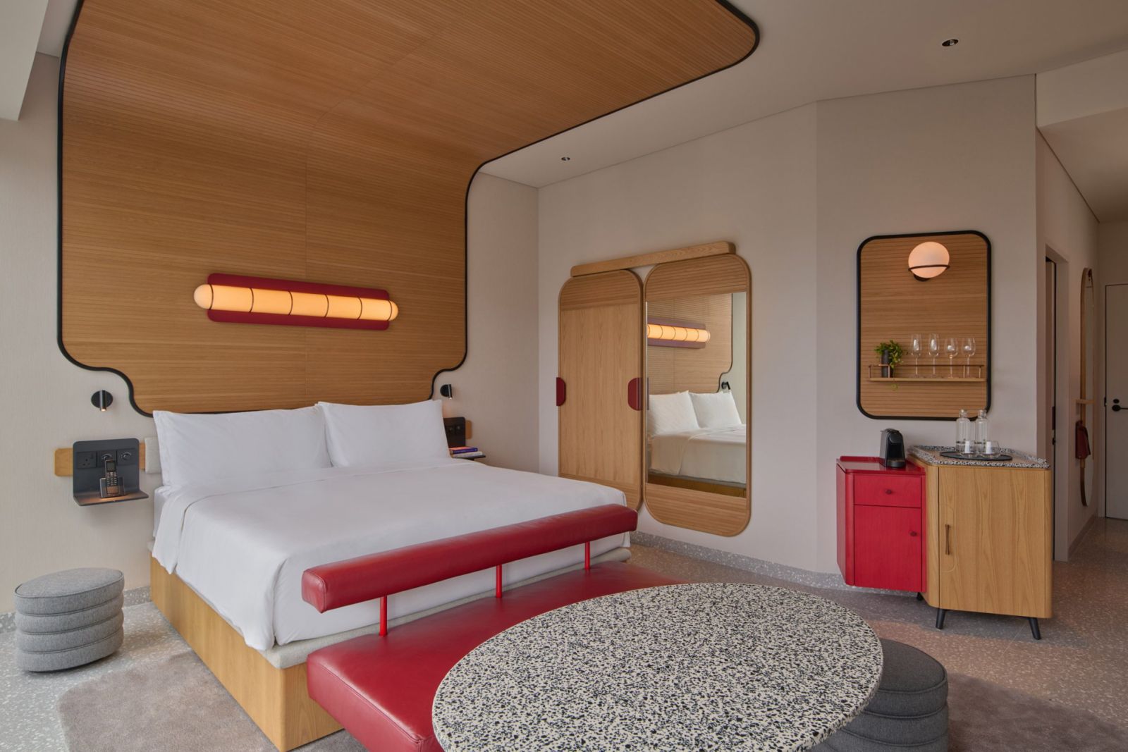 Guest room at The Standard Singapore featuring sculptural oak paneling, cylindrical light fixture, and modernist red accents—showcasing the hotel's signature approach to mid-century inspired design (Photo: The Standard Singapore)