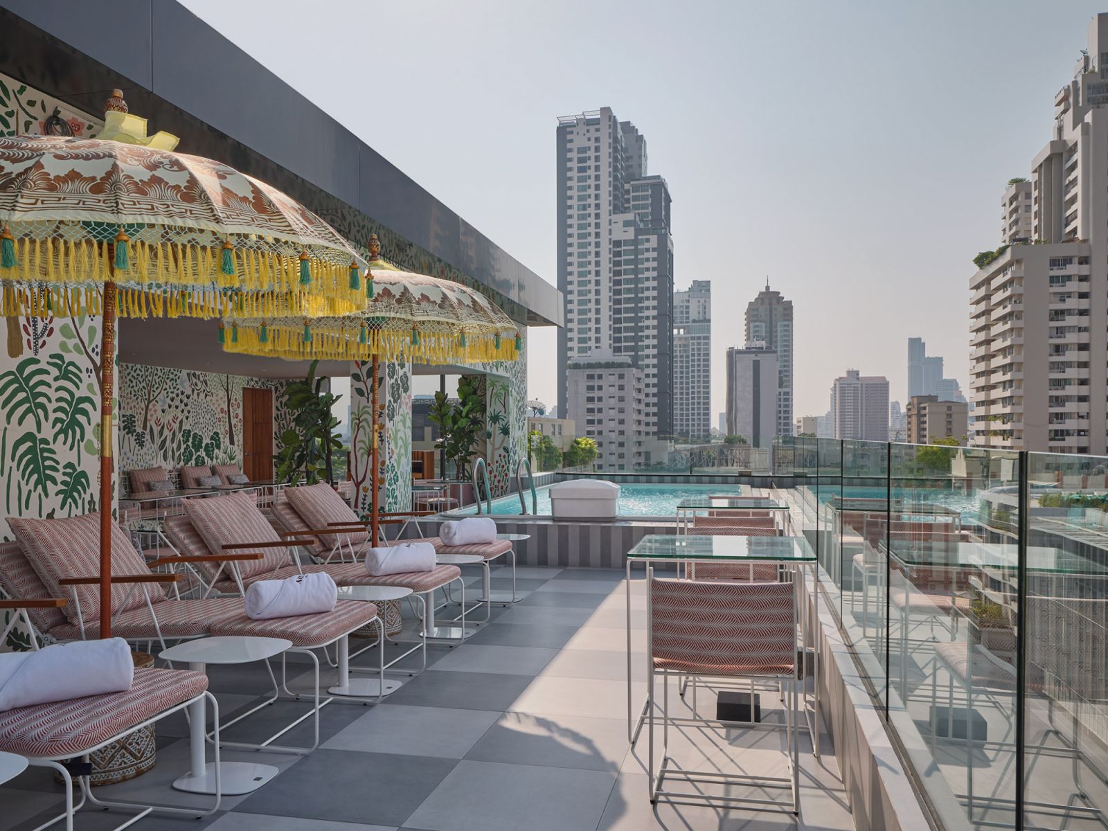 Poolside terrace at Public House Hotel Bangkok with decorative umbrellas, hand-painted botanical murals, and skyline views—merging mid-century modern aesthetics with traditional Thai craftsmanship  (Photo: Public House Hotel Bangkok)