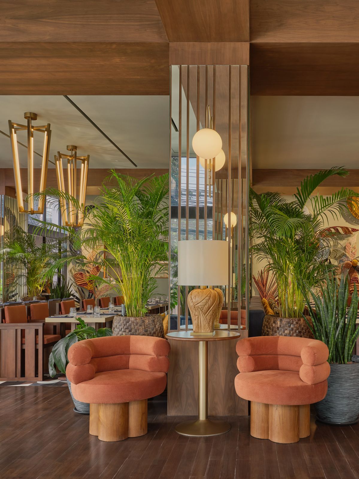 Coral-hued lounge chairs at Public House Hotel Bangkok surrounded by lush tropical plants and walnut paneling, showcasing the property's signature combination of mid-century forms and warm materials (Photo: Public House Hotel Bangkok)