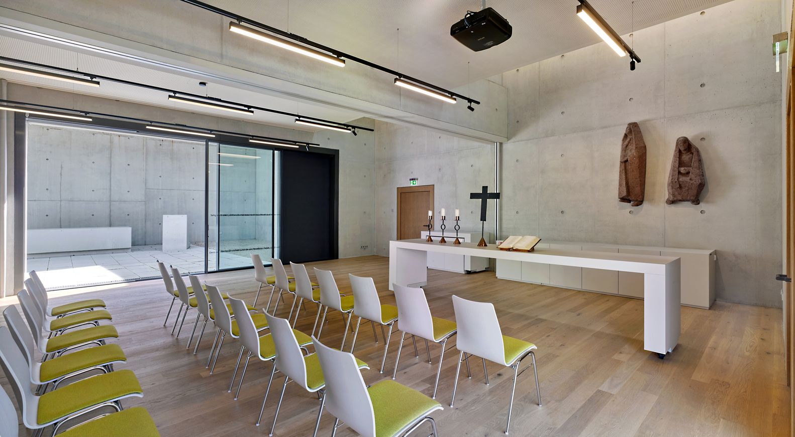 Contemporary parish hall interior with wooden floors, white and chartreuse chairs, and glass partitions connecting to the outer church space (Photo: Meixner Schlüter Wendt)