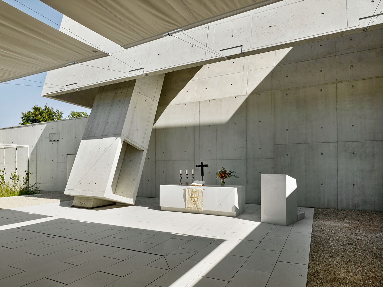 Minimalist altar space with fair-faced concrete walls, where the sloping skylight casts light onto the simple white altar below (Photo: Meixner Schlüter Wendt)
