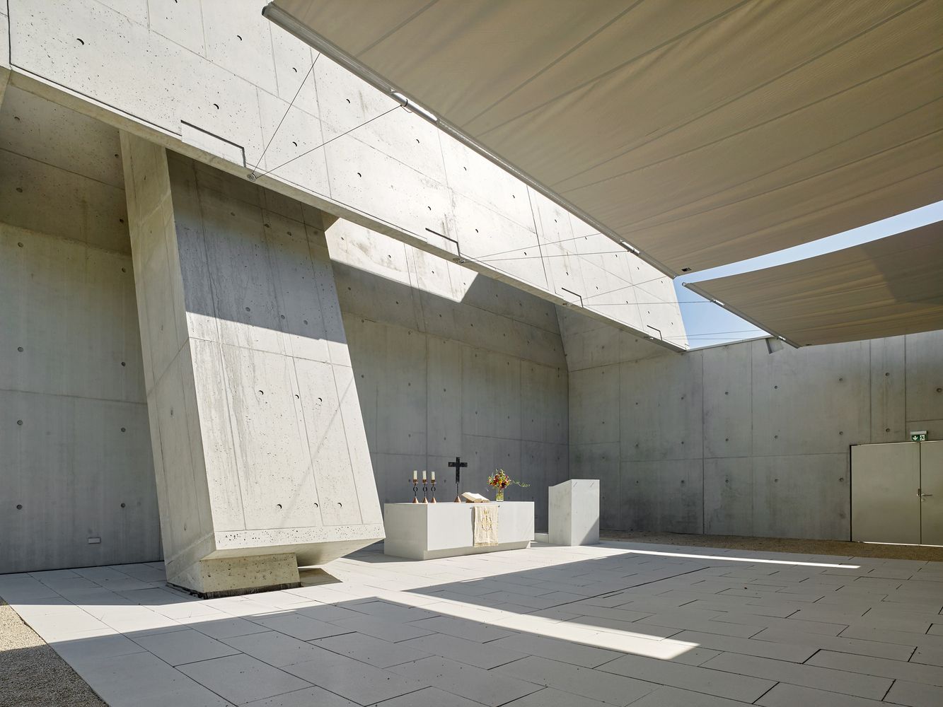 Another perspective of the outer church showcasing concrete forms, fabric canopies, and the minimalist white altar beneath carefully orchestrated natural light (Photo: Meixner Schlüter Wendt)