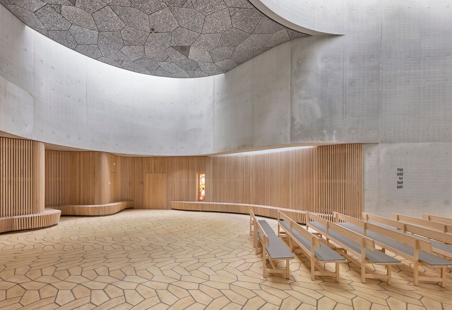 Ash wood seating and wall paneling contrast with concrete walls while pentagonal floor tiles extend the geometric pattern from ceiling to ground (Photo: Rørbæk og Møller Arkitekter)