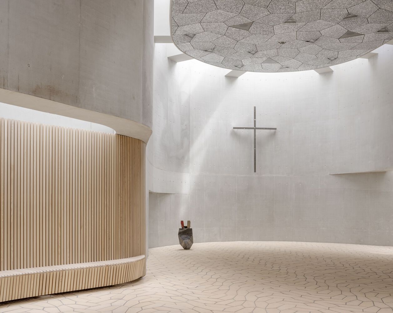 Interior view showing pentagonal floor tiles, aluminum ceiling and minimalist cross mounted on concrete wall beneath dramatic skylight (Photo: Rørbæk og Møller Arkitekter)