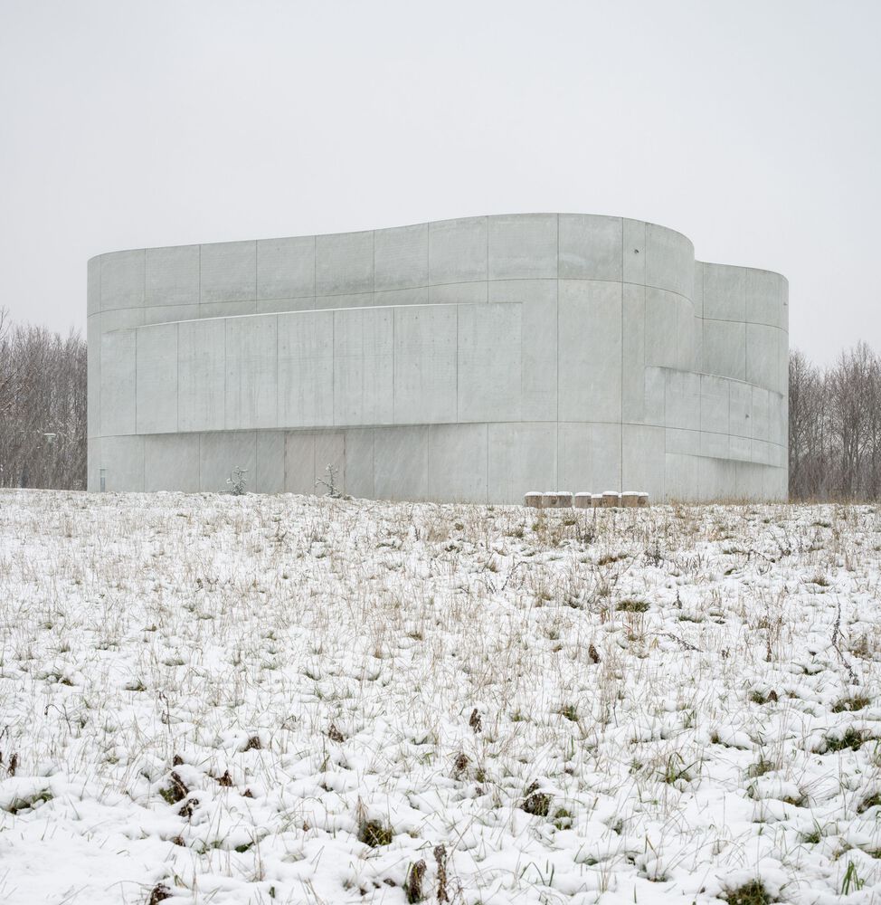 Exterior view of Trekroner Church in winter, showing the curved concrete structure created from nine custom-cast sections. The organic form stands distinct against the snow-covered landscape (Photo: Rørbæk og Møller Arkitekter)