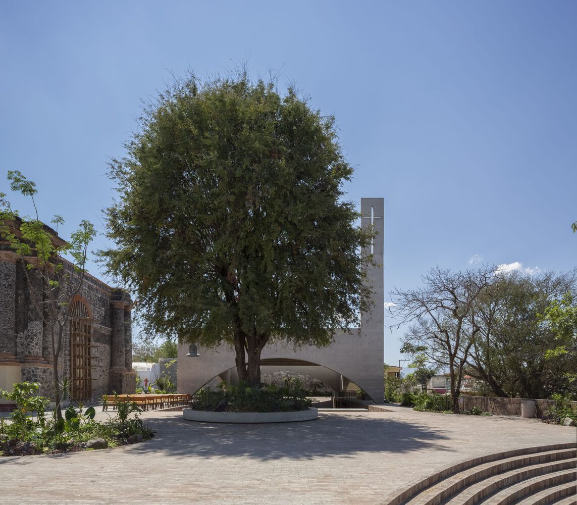 Entry plaza with a preserved tree at its center, showing the relationship between the new concrete sanctuary and remnants of the historic stone structure damaged in the 2017 earthquake (Photo: Dellekamp Schleich + AGENdA Agencia de Arquitectura)