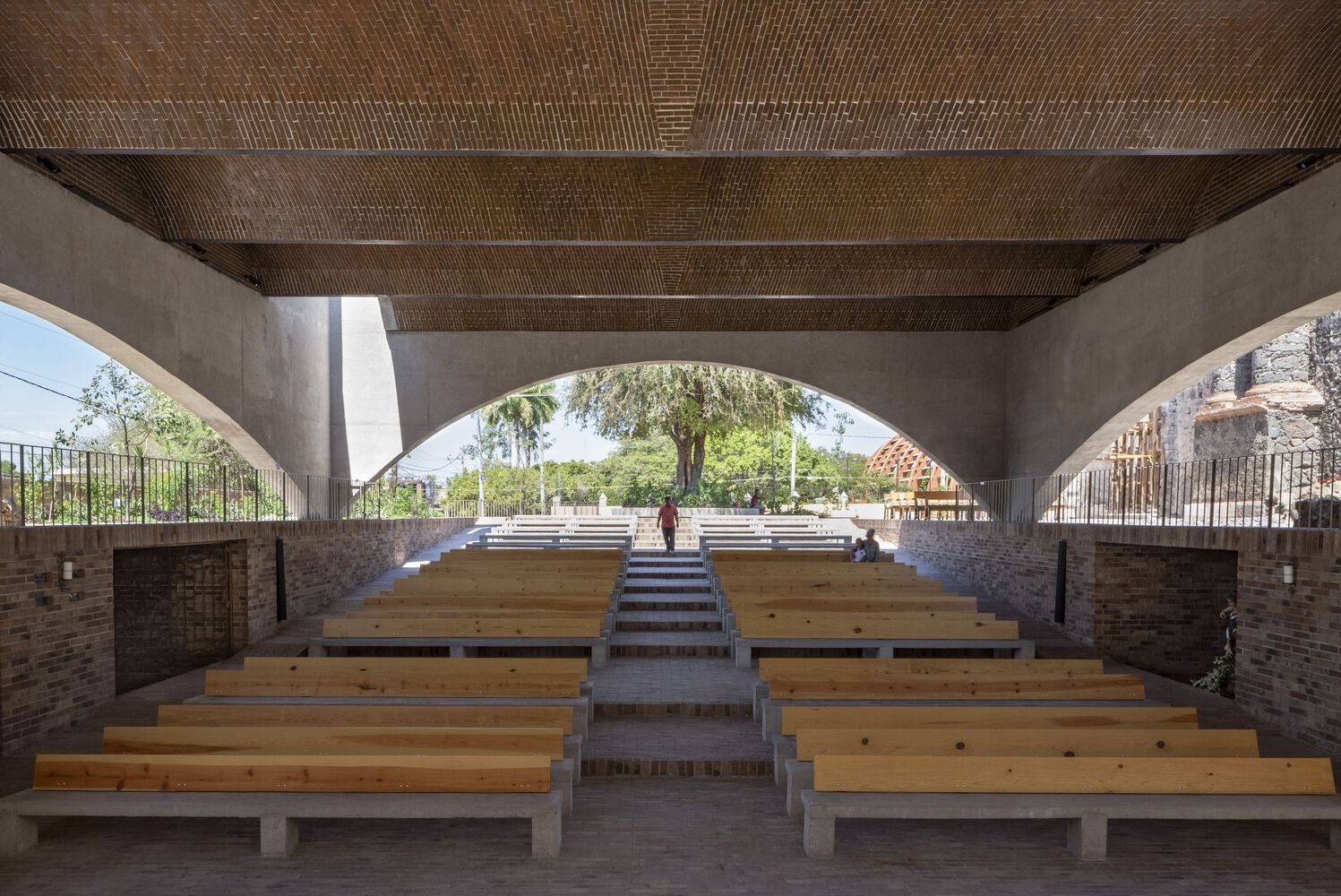 Looking outward from inside the sanctuary, with wooden pews arranged on a gentle slope leading to the altar area. The brick-vaulted ceiling provides both shelter and openness (Photo: Dellekamp Schleich + AGENdA Agencia de Arquitectura)