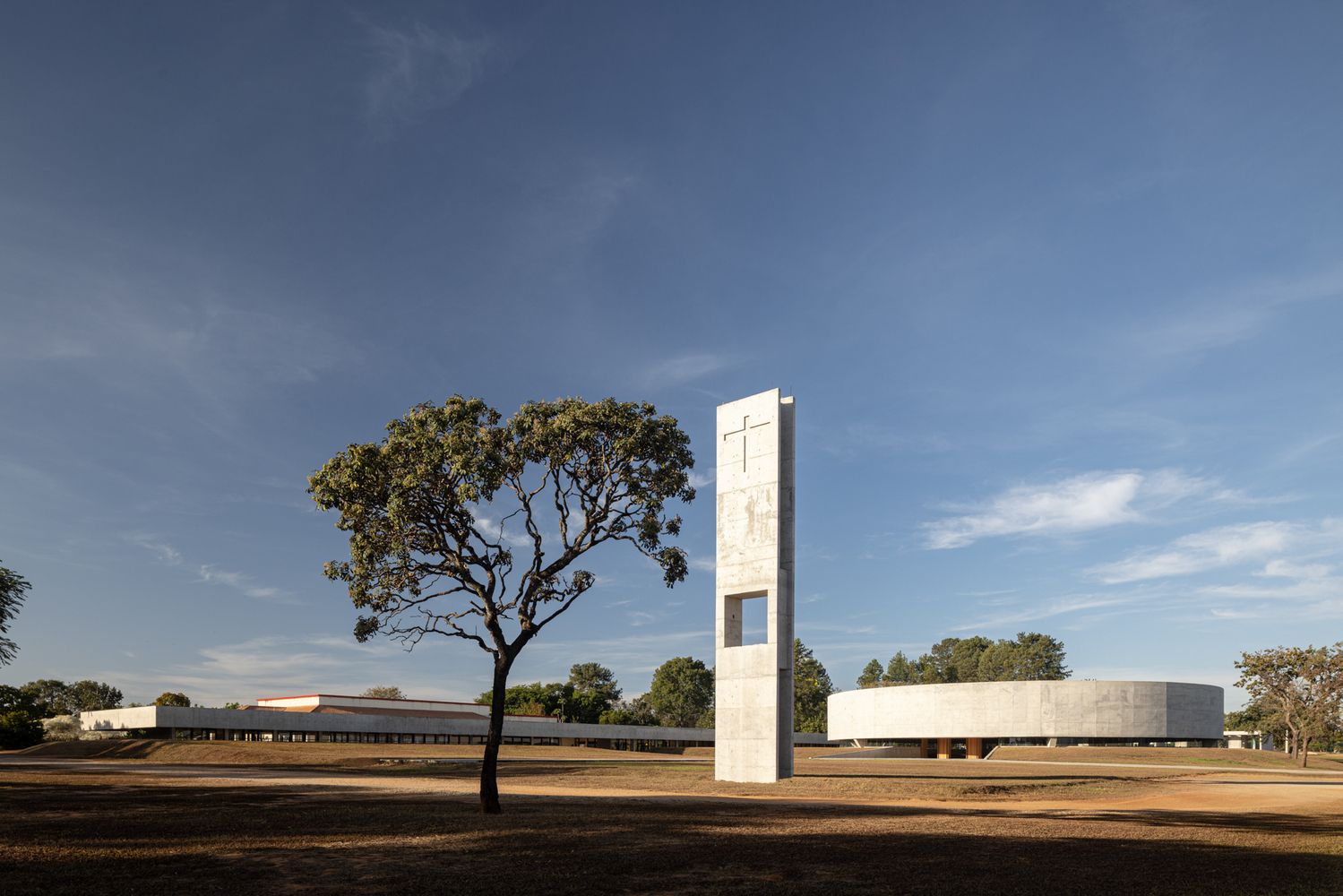 Another perspective of the church complex displaying the relationship between the circular worship space and rectangular community buildings, with the vertical bell tower as a visual anchor (Photo: ARQBR Arquitetura e Urbanismo)
