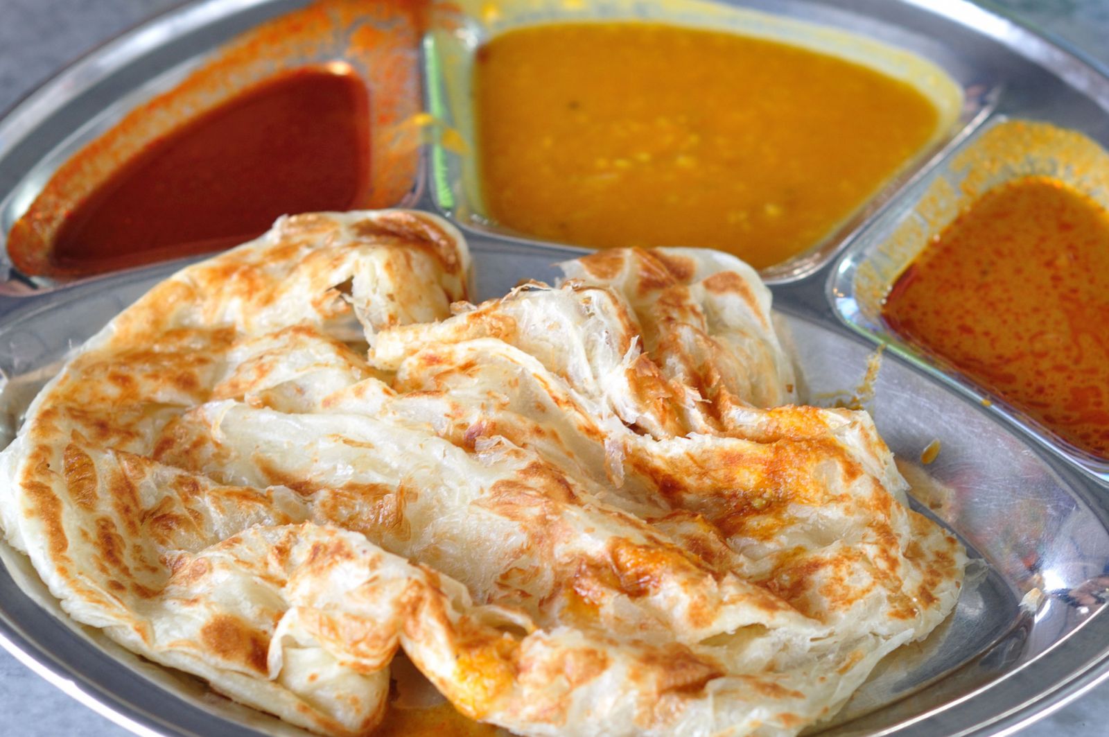 Roti canai, a universally loved meal of flaky flatbread with an array of curries and dahls