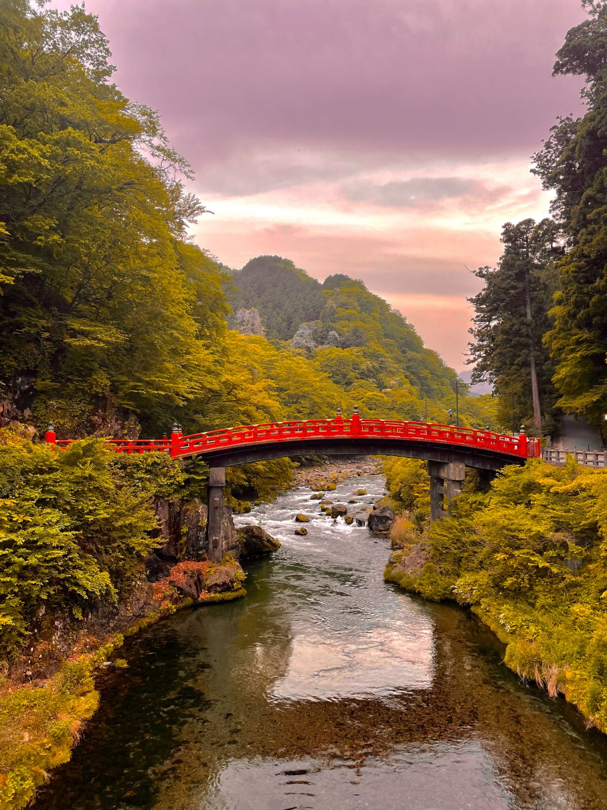 A traditional Japanese bridge over a river with mountains and trees in the background