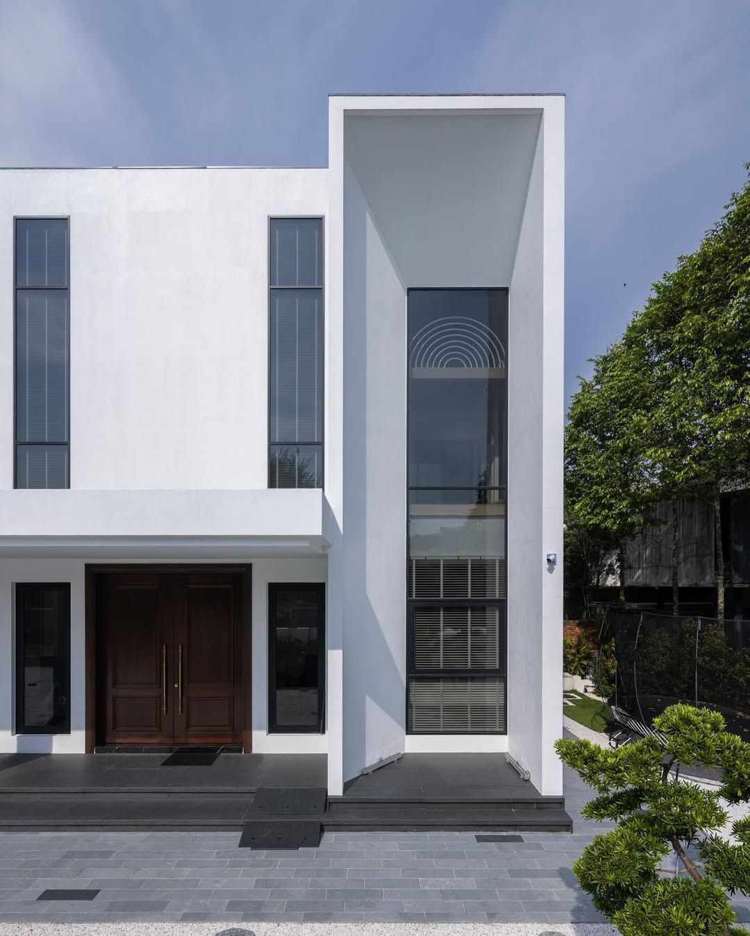 The entrance has rich wooden doors contrasting against pristine white volumes and meticulous landscaping