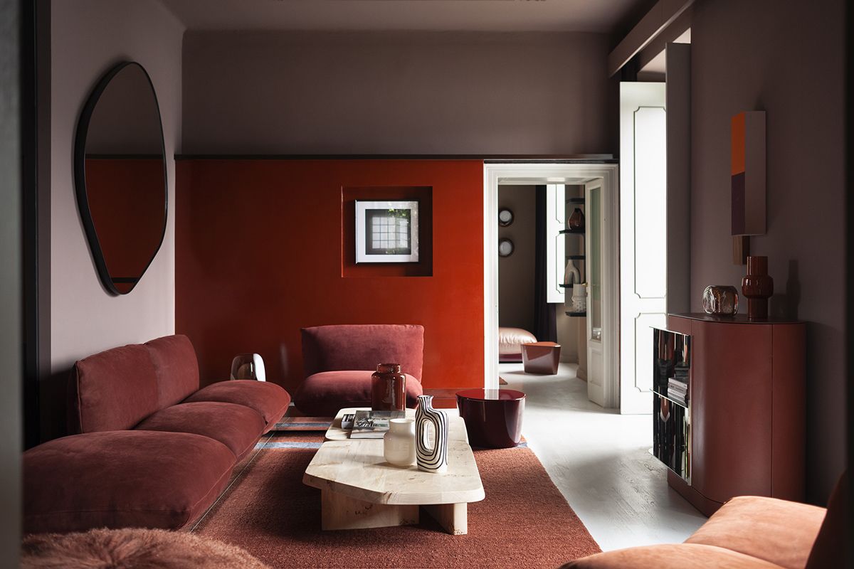 A red-hued room featuring Baxter Aura sofa and Aegates small table