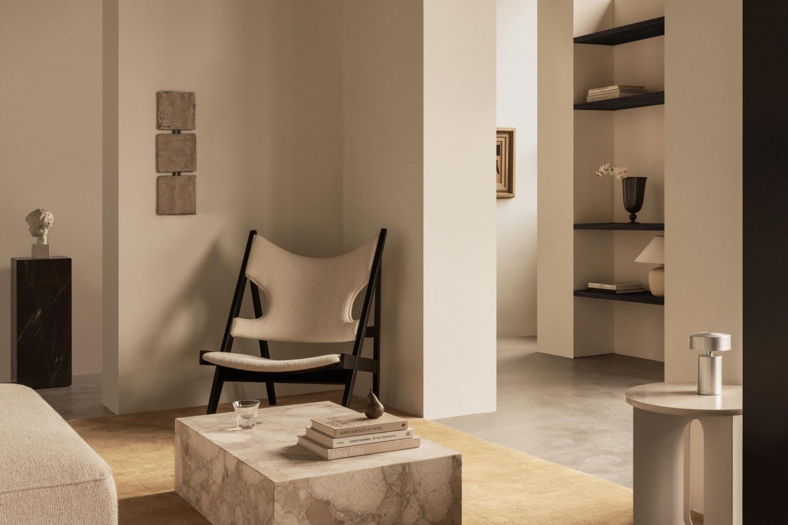 A sculptural chair and marble coffee table serve as functional art pieces, while recessed shelving creates depth without disrupting the room’s serene composition (Photo: Audo)