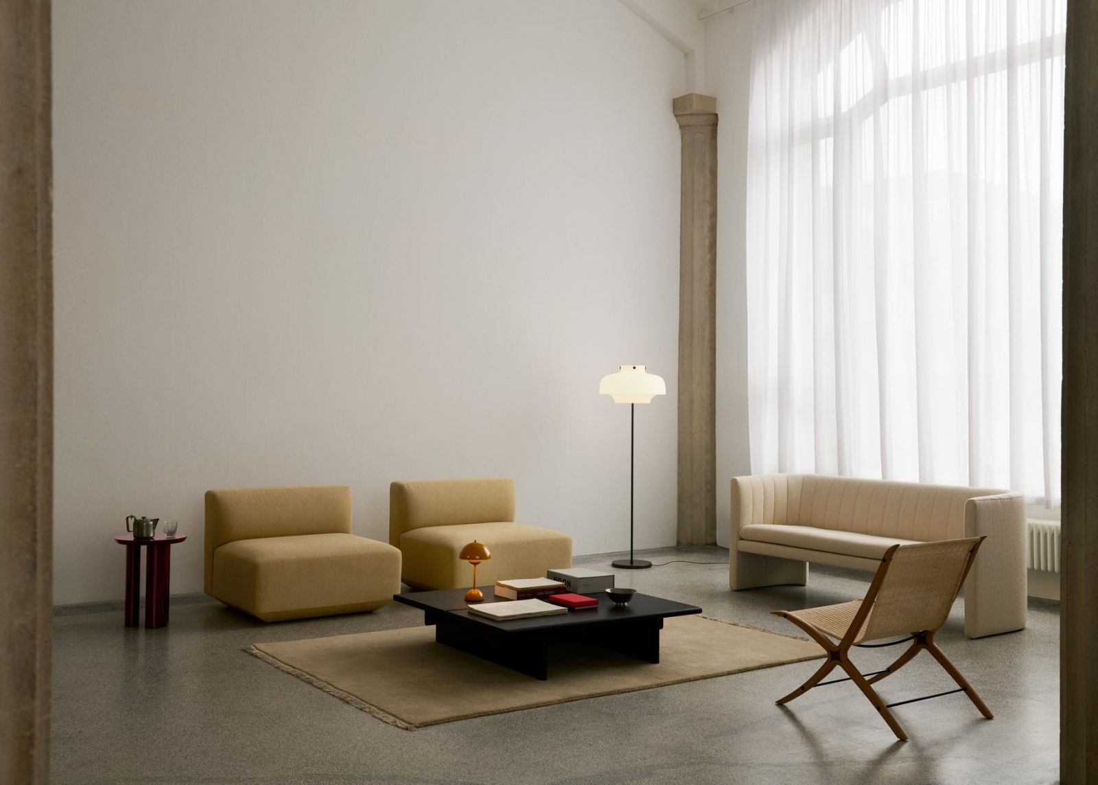 The restrained furniture arrangement features sculptural modular seating in soft buttery tones, while the woven folding chair introduces subtle textural contrast (Photo: &Tradition)