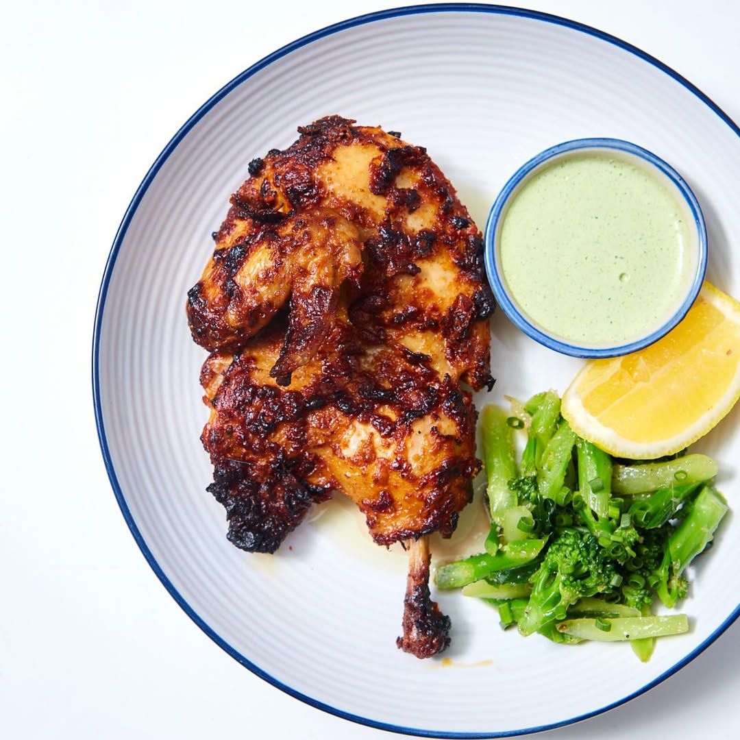 Harissa Spring Chicken ไก่จากราชบุรีย่างจนหนังกรอบ เนื้อนุ่มฉ่ำ เสิร์ฟพร้อมผักย่าง ซอสสไตล์เปรู และเลมอนสด จากร้าน Unscene Wine Bar (ภาพ: Instagram / @unscenebkk)