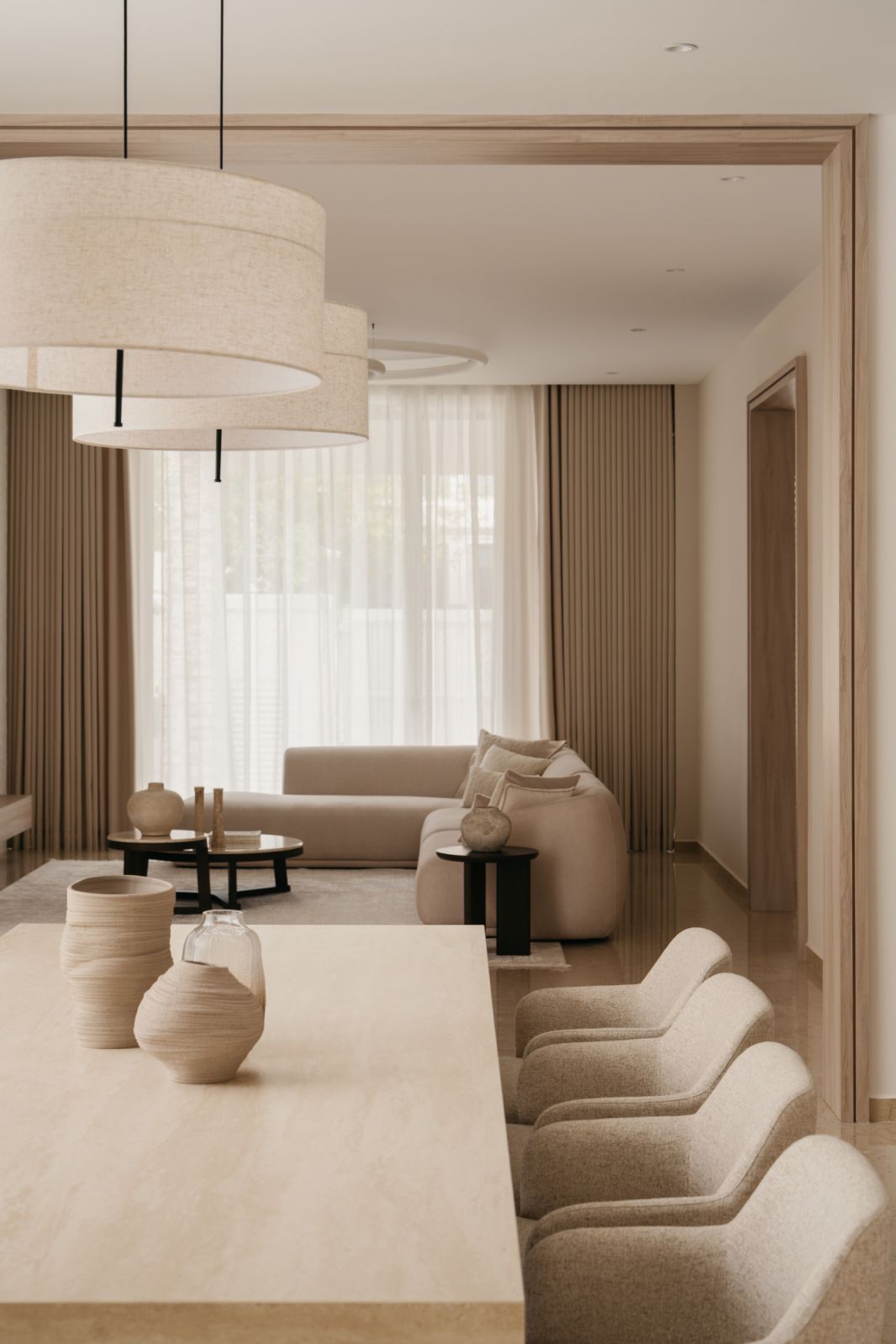 Layered lighting design with fabric pendants illuminating bespoke limestone dining table and artisanal ceramic vessels in neutral dining space