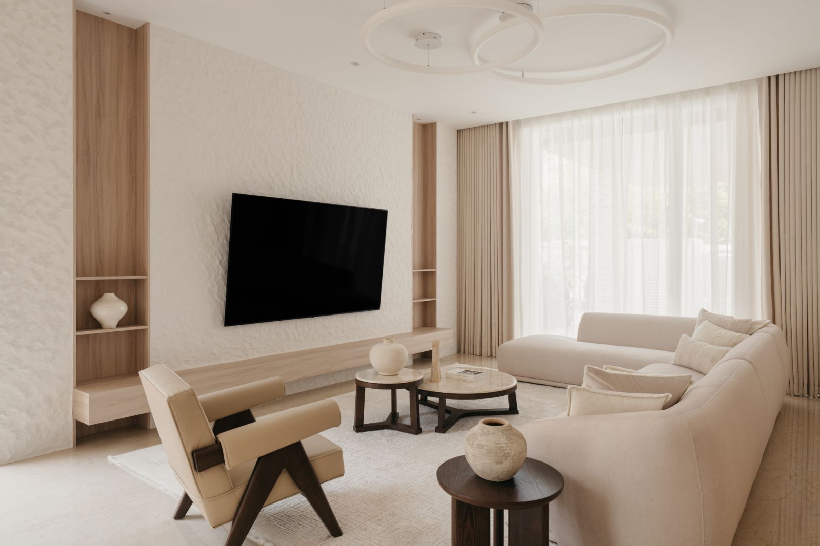 Contemporary living room with textured wall treatment, circular LED pendant light and bespoke curved seating in neutral Aman-inspired palette